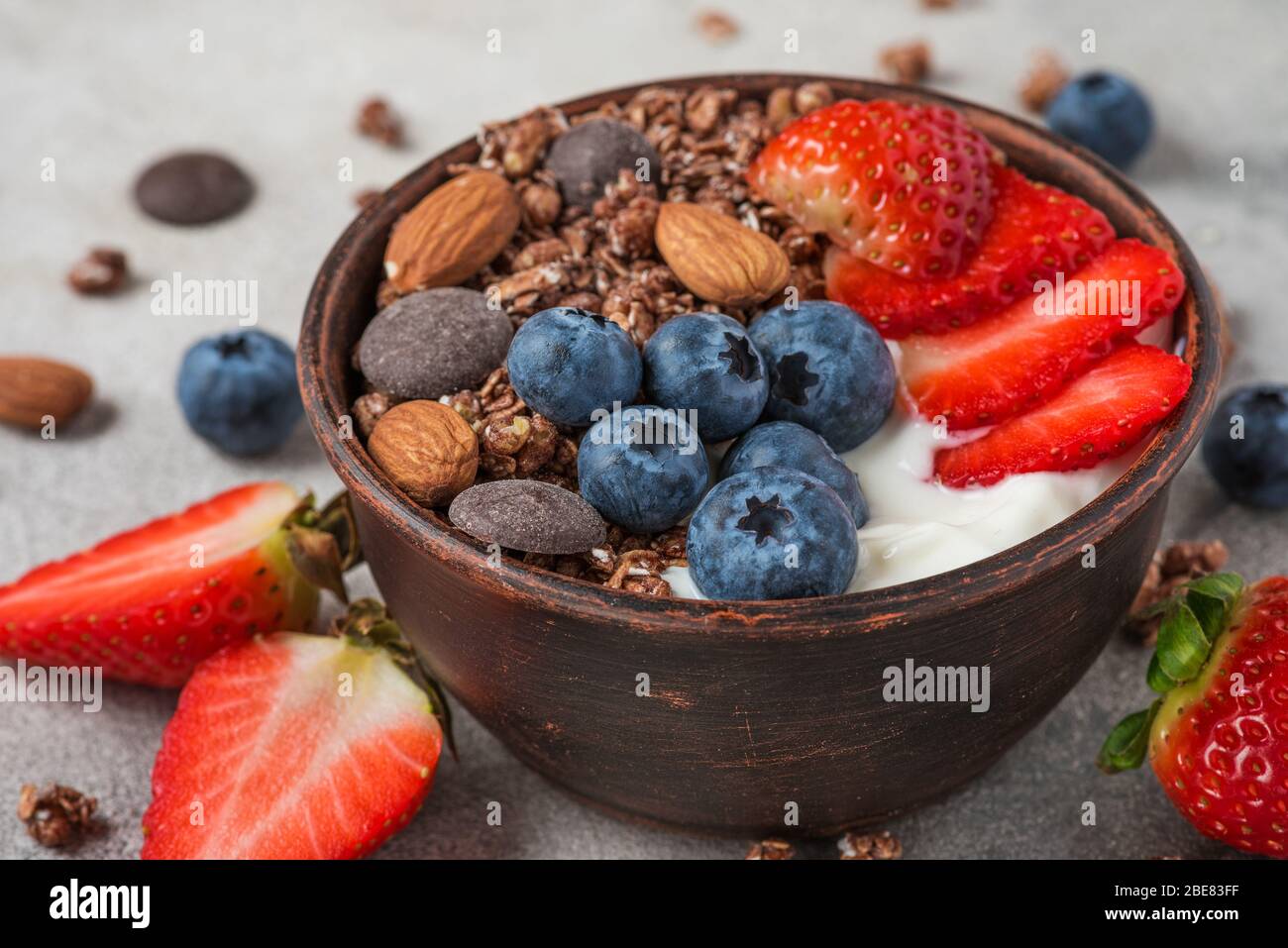 bowl of oat chocolate granola with yogurt, fresh blueberries, strawberries and nuts on gray background for healthy breakfast. close up Stock Photo