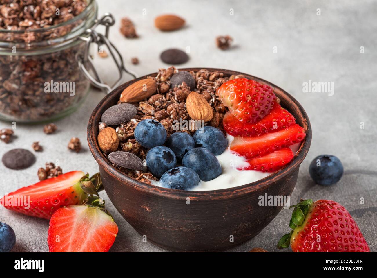 chocolate granola with greek yogurt, fresh berries and nuts in a bowl on gray background for healthy breakfast. close up Stock Photo