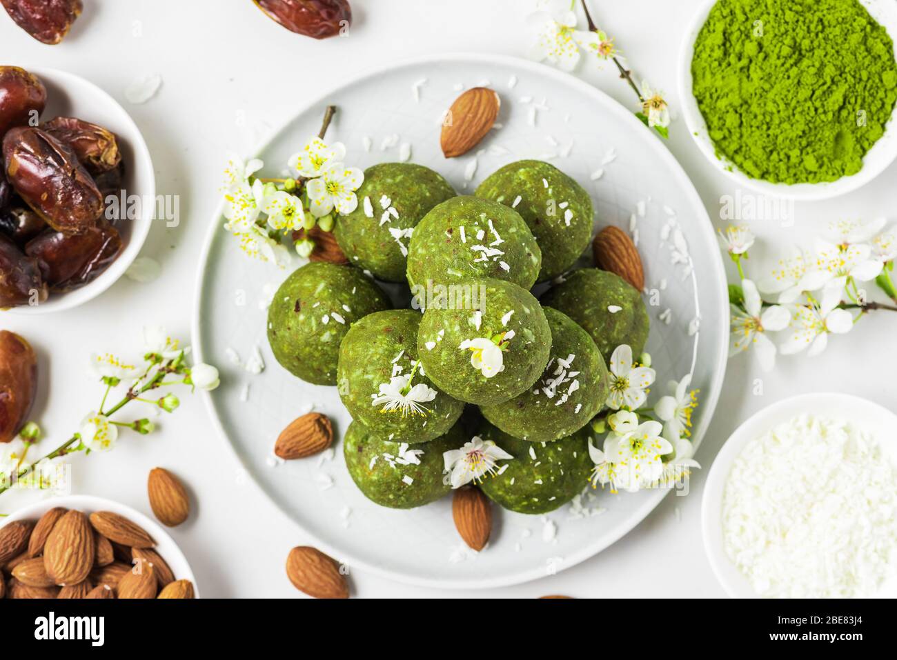 Homemade raw energy balls made of green matcha tea, dates and nuts with spring flowers. Top view