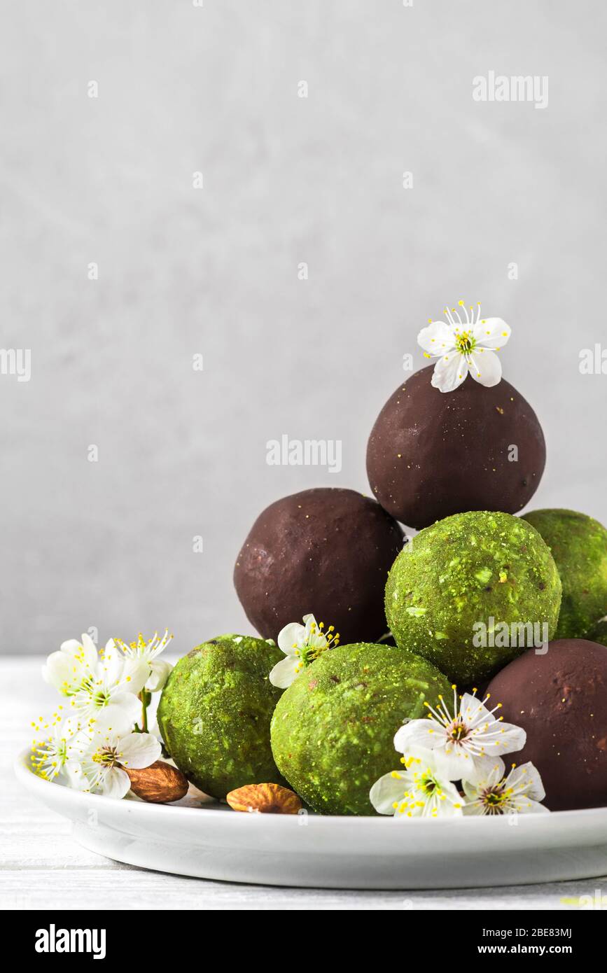 Raw vegan energy balls made of matcha tea, dates and nuts and balls in chocolate glaze with spring blossom flowers. Food styling. Healthy vegan desser Stock Photo