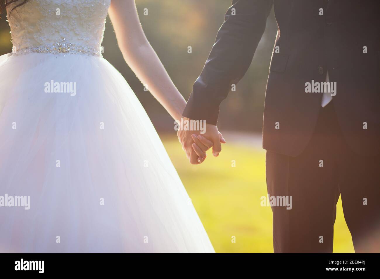 Back view of bride in white dress and groom in suit holding each others ...