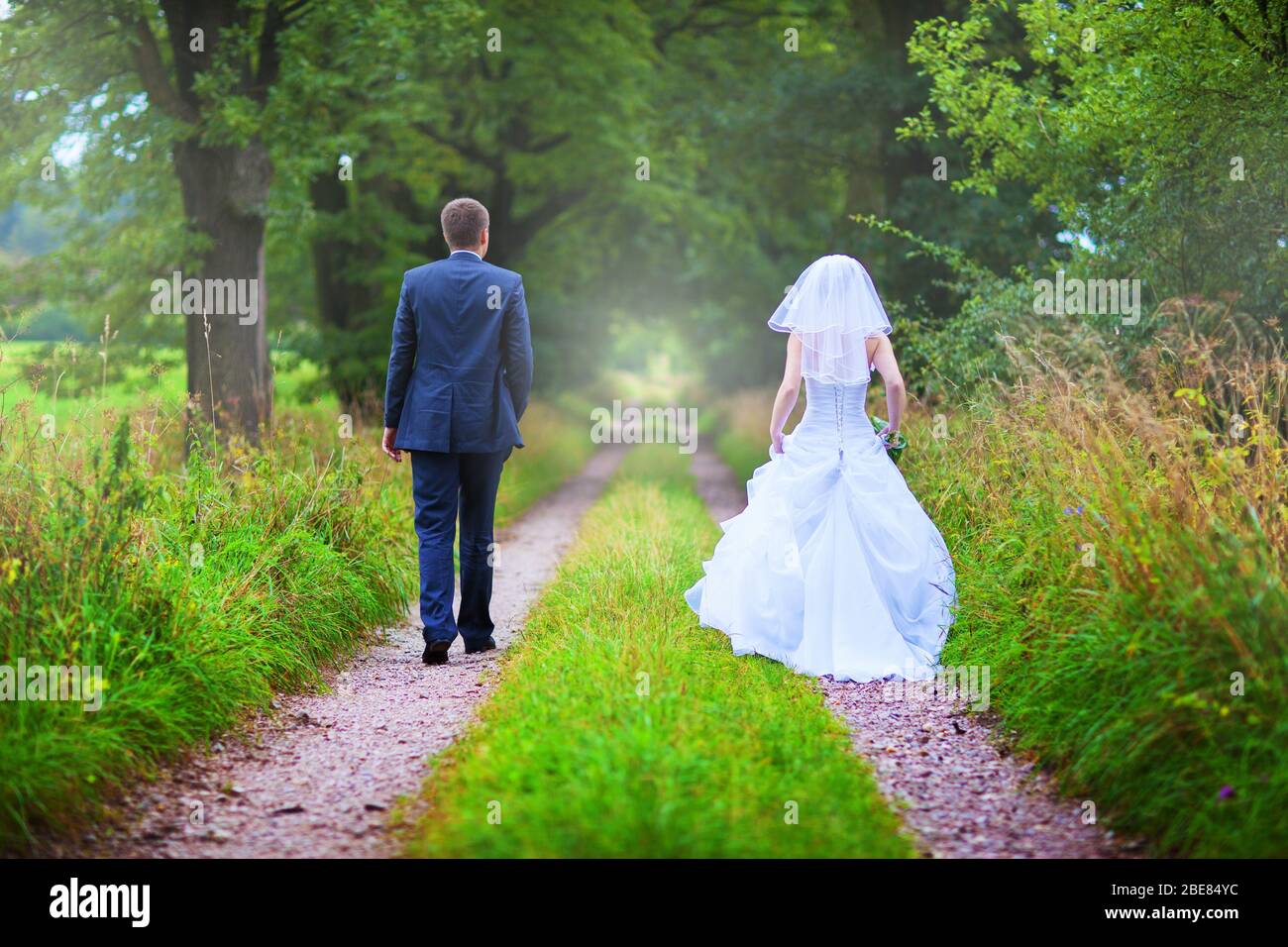 Back view of bride in white dress and groom in suit holding each others ...