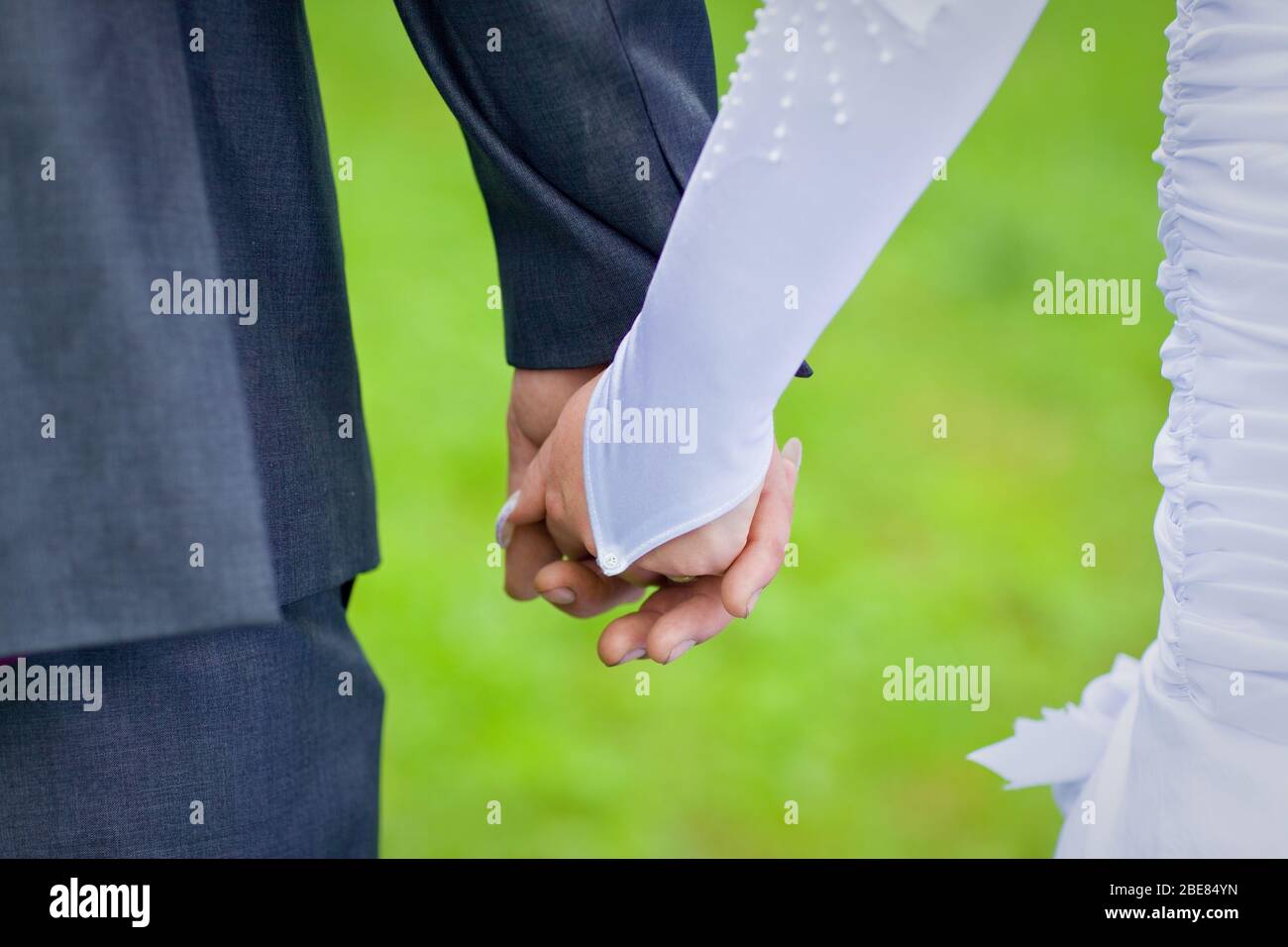 Back view of bride in white dress and groom in suit holding each others ...