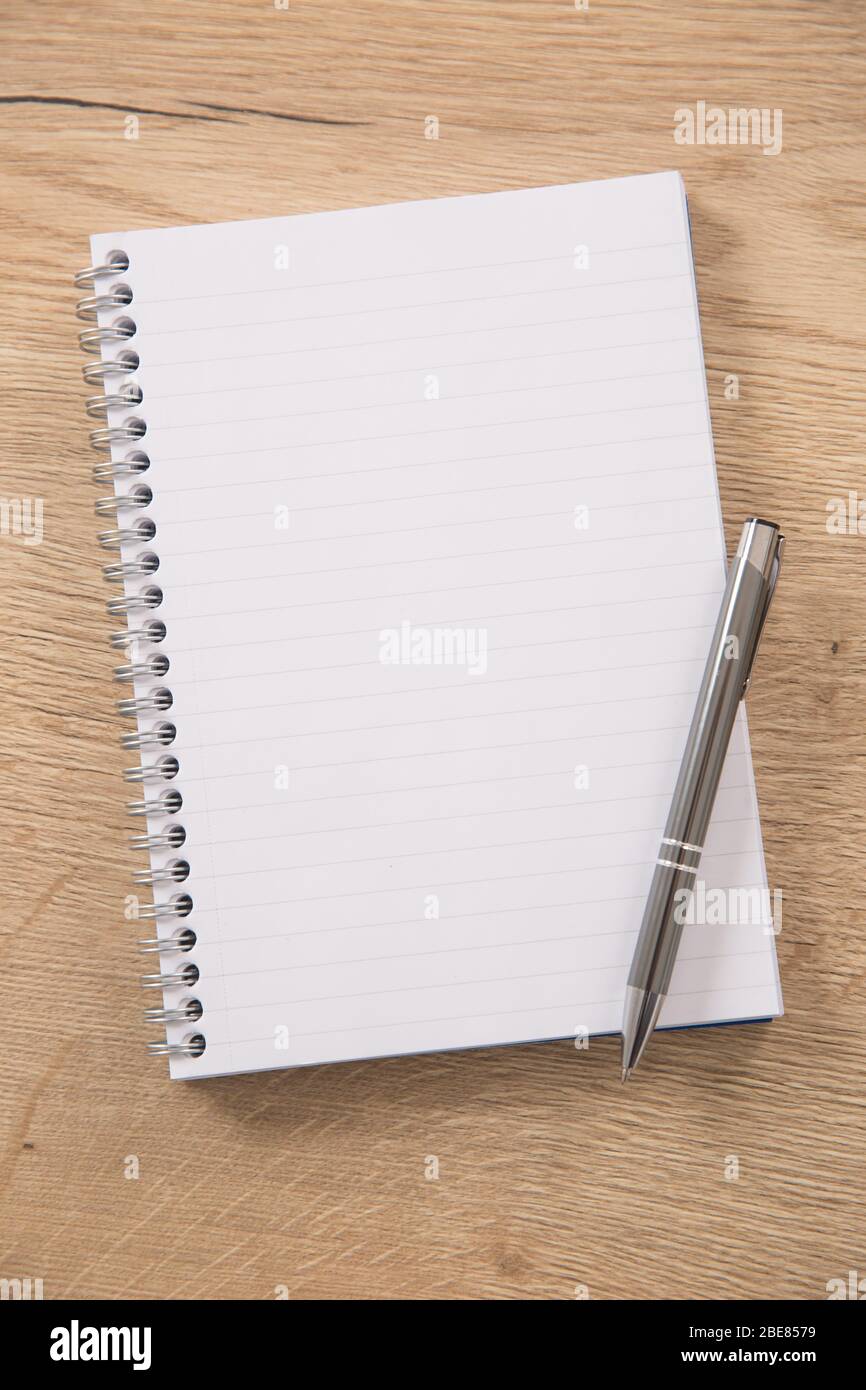 White lined notepad with a metal ring wire binding and a silver pen opened on a wooden surface. Stock Photo
