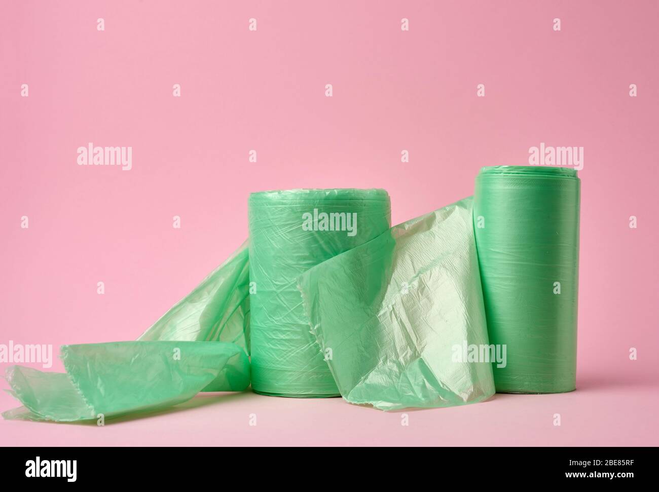 two rolls green plastic bags for trash bin on pink background, close up Stock Photo