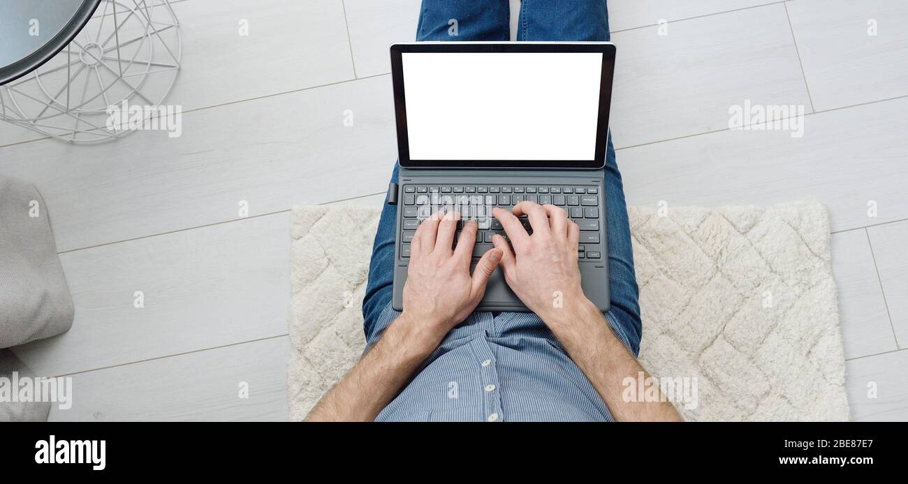 Top view of young man in casual clothes sitting on floor and working on his mockup laptop computer at home. Stay home and work online. Quarantine Stock Photo