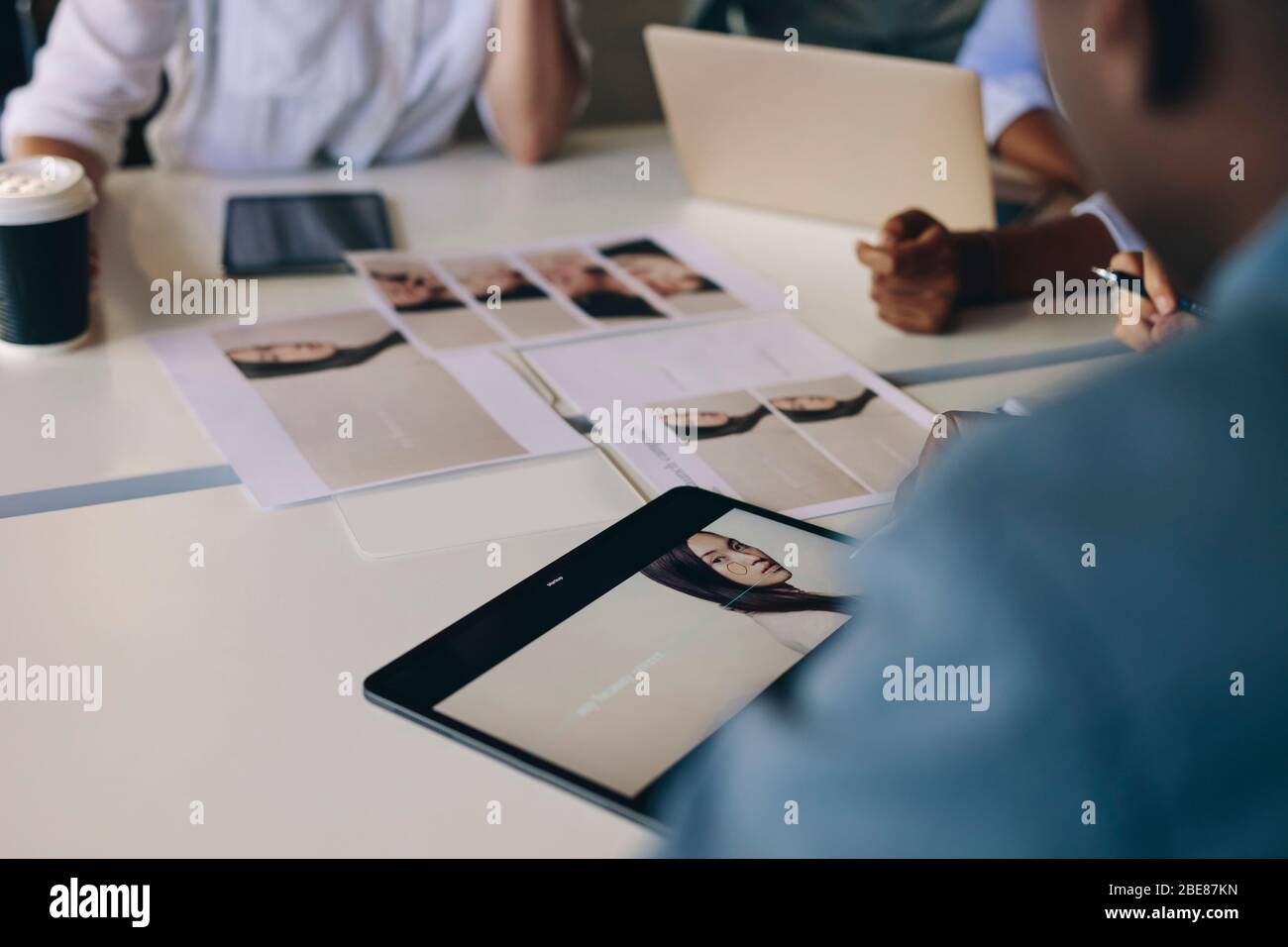 Group of business people selecting material for a project sitting around a table with photo on digital tablet and photo prints. Stock Photo