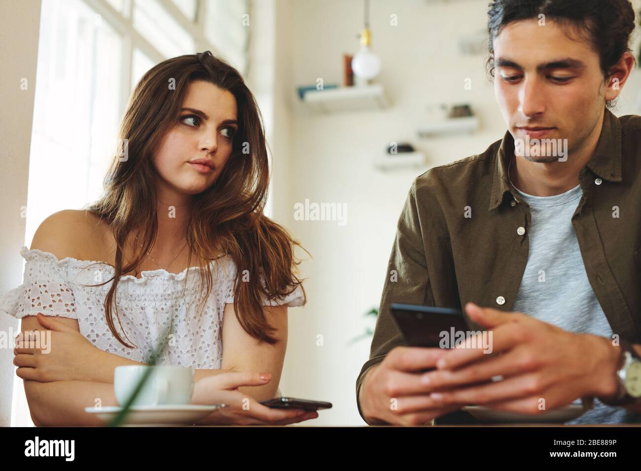Woman looking unhappy while her man paying no attention to her and busy using his mobile phone. Sulking woman sitting next to man reading text message Stock Photo