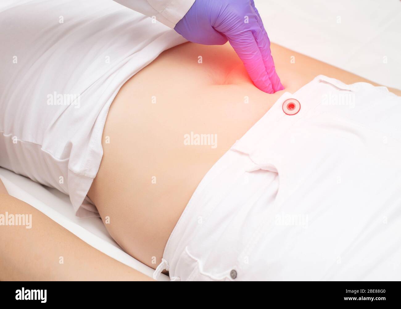 A traumatologist doctor examines the lower abdomen of a girl who has a blunt abdominal injury, stomach ulcer Stock Photo