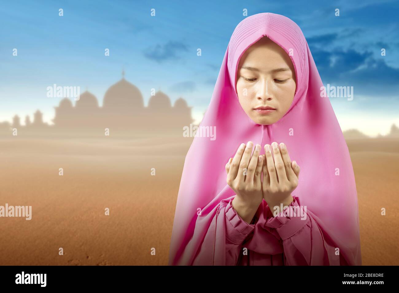 Asian Muslim woman in a veil standing while raised hands and praying on ...