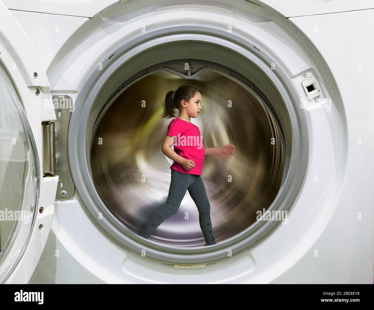 Kid runs inside washing machine, little girl doing fitness training during COVID-19 quarantine. Child exercises staying at home due to coronavirus pan Stock Photo