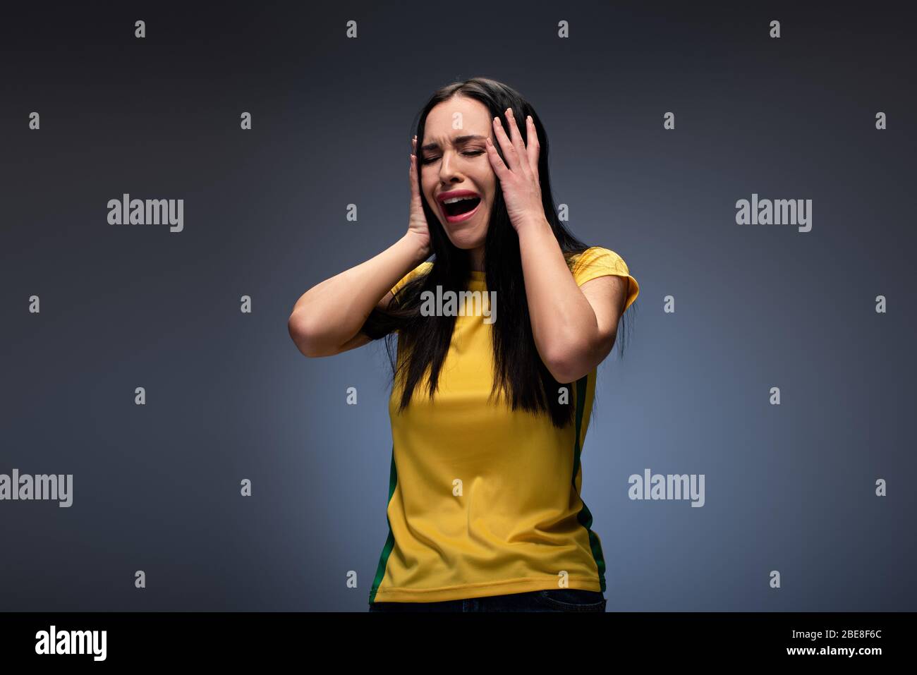 stressed attractive young woman crying and holding head on grey Stock Photo