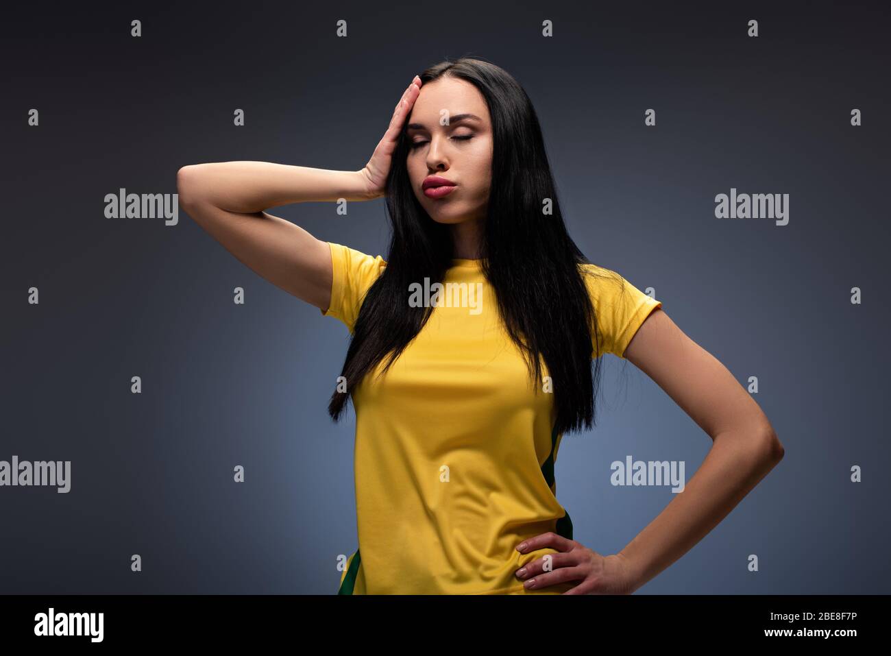 tired young woman in yellow t-shirt holding head on grey Stock Photo
