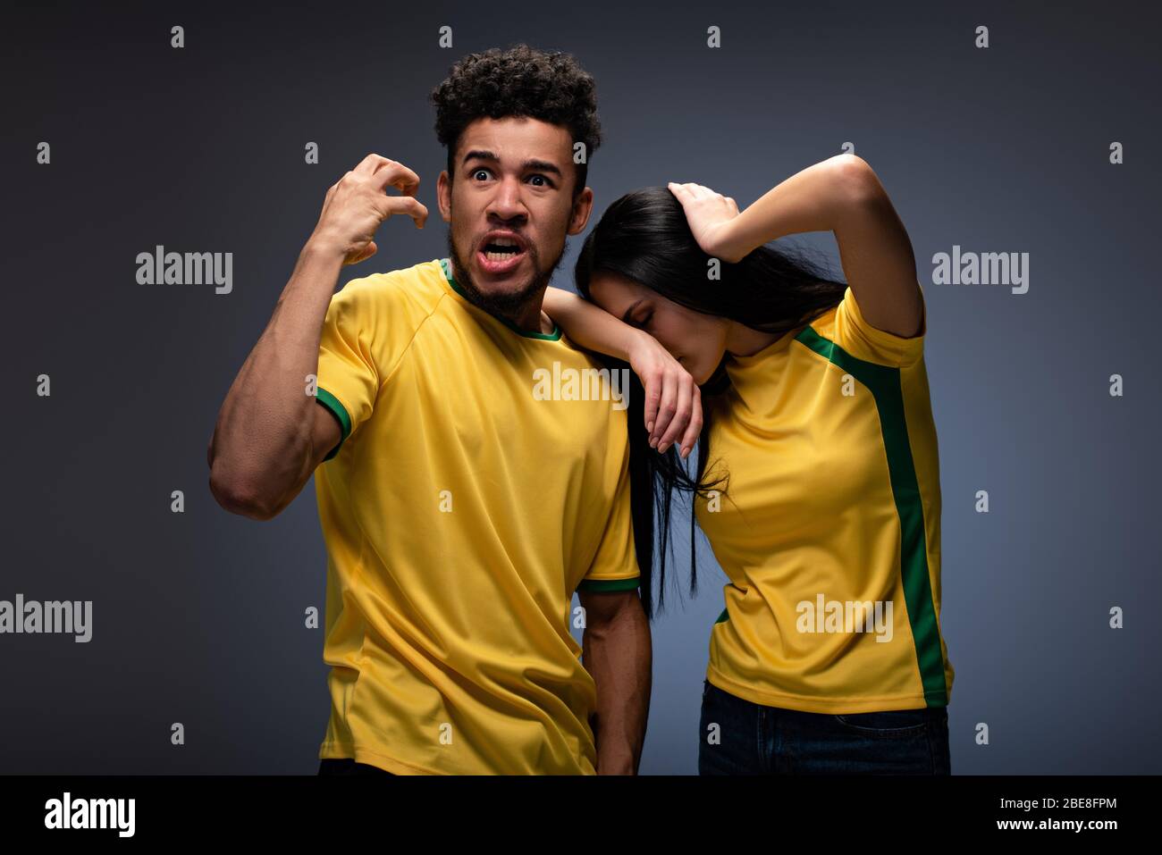 multiethnic couple of angry football fans in yellow tshirts gesturing