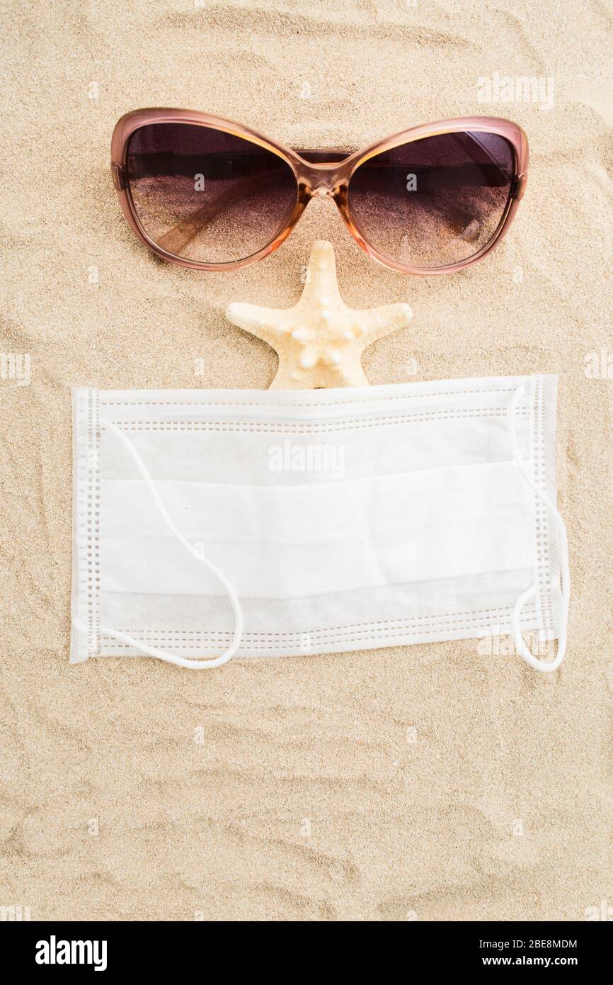 Funny face of safety vacation concept with sunglasses, medicine ask and sea star on sand. Top view. Copy space. Flat lay Stock Photo