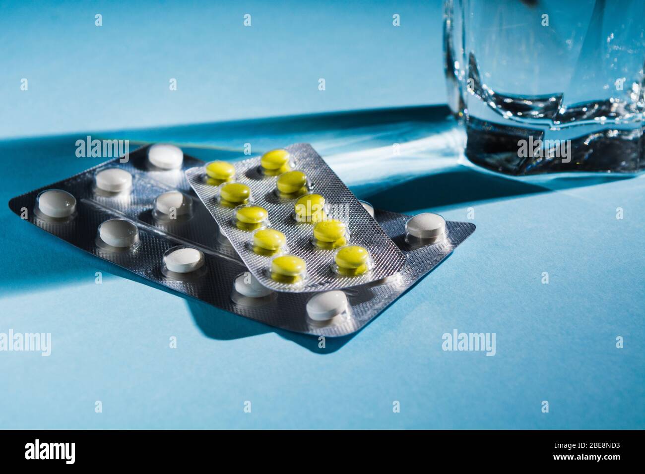 Two blister of pills with glass of water over blue background. Soft focus. Copy space. Tablets against pain or flu Stock Photo