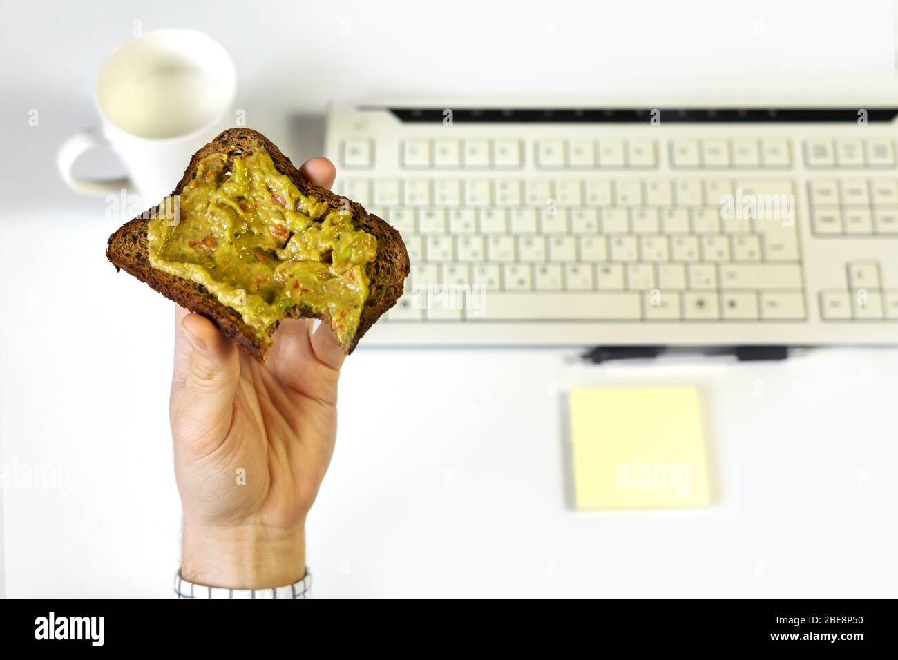 Busy business man eating healthy avocado toast breakfast in a hurry while working on computer Stock Photo