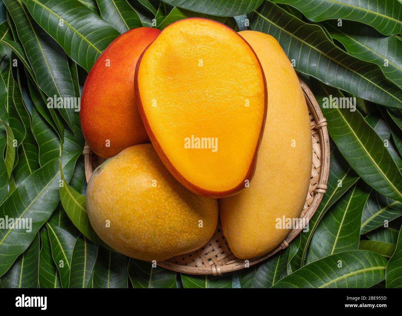 Mango, tropical fruit, in a bamboo wooden sieve basket on green leaf ...