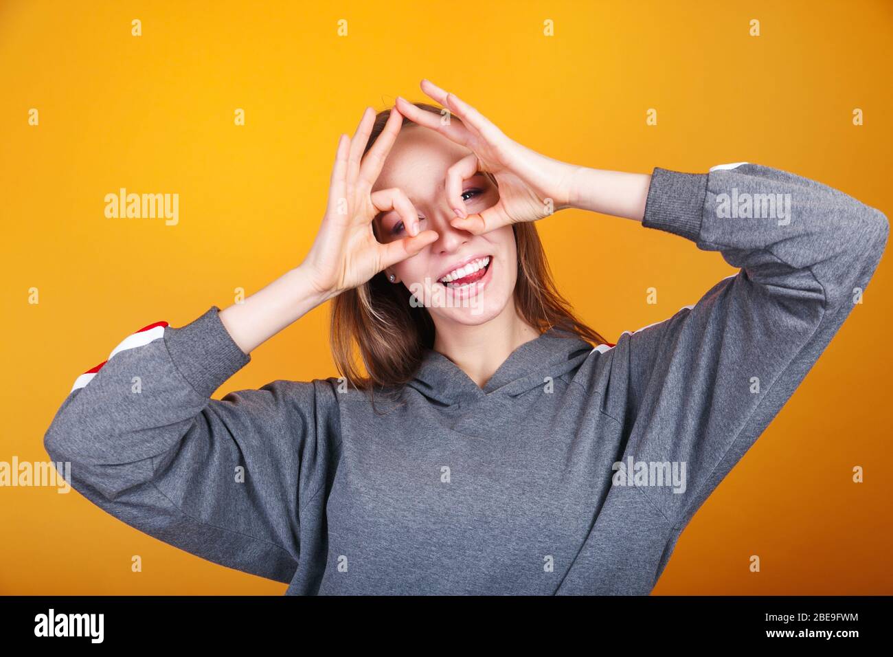 Close up portrait of attractive gorgeous charming girl hands in specs form near eyes on yellow background Stock Photo