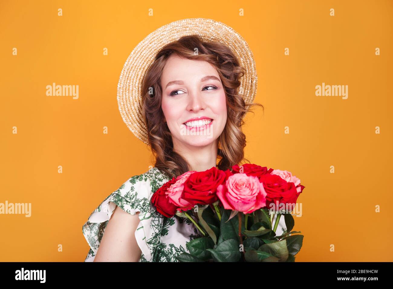 Portrait of romantic young girl in dress and straw hat holding roses ...