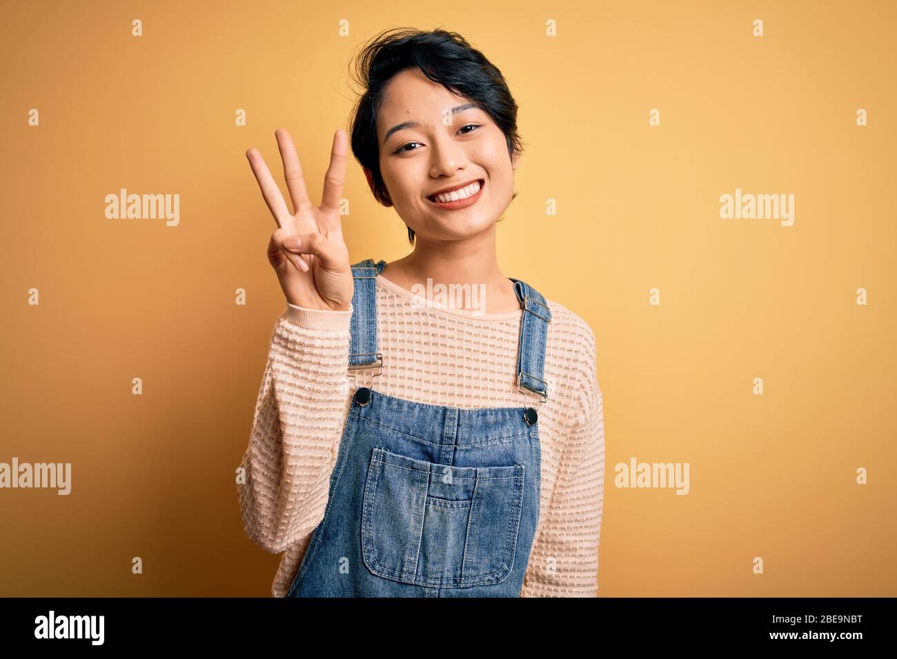 Young beautiful asian girl wearing casual denim overalls over isolated ...