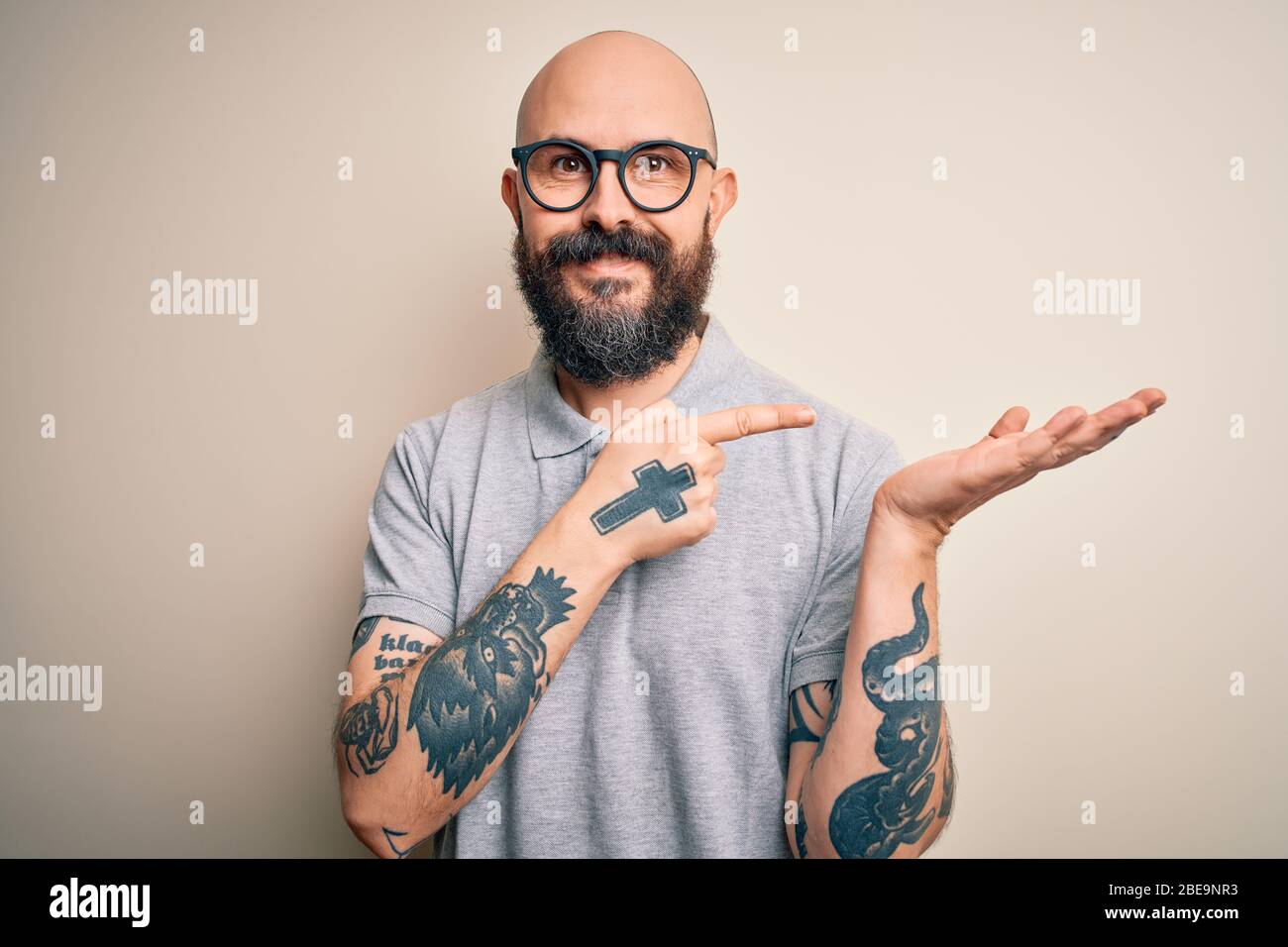 Handsome bald man with beard and tattoo wearing casual polo and glasses  amazed and smiling to the camera while presenting with hand and pointing  with Stock Photo - Alamy