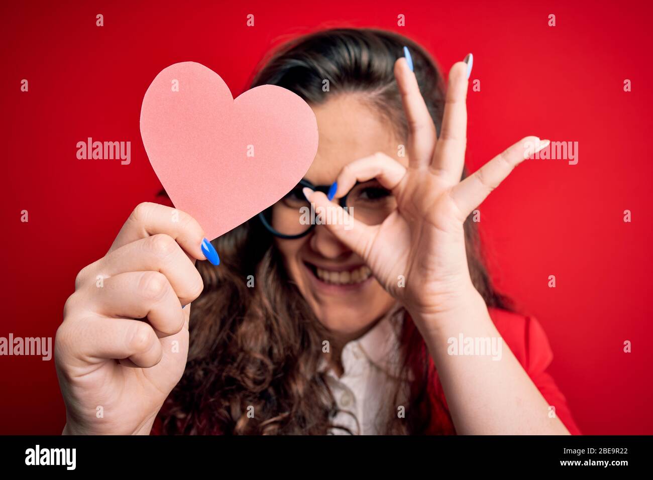 Young beautiful woman with curly hair holding paper heart over isolated ...