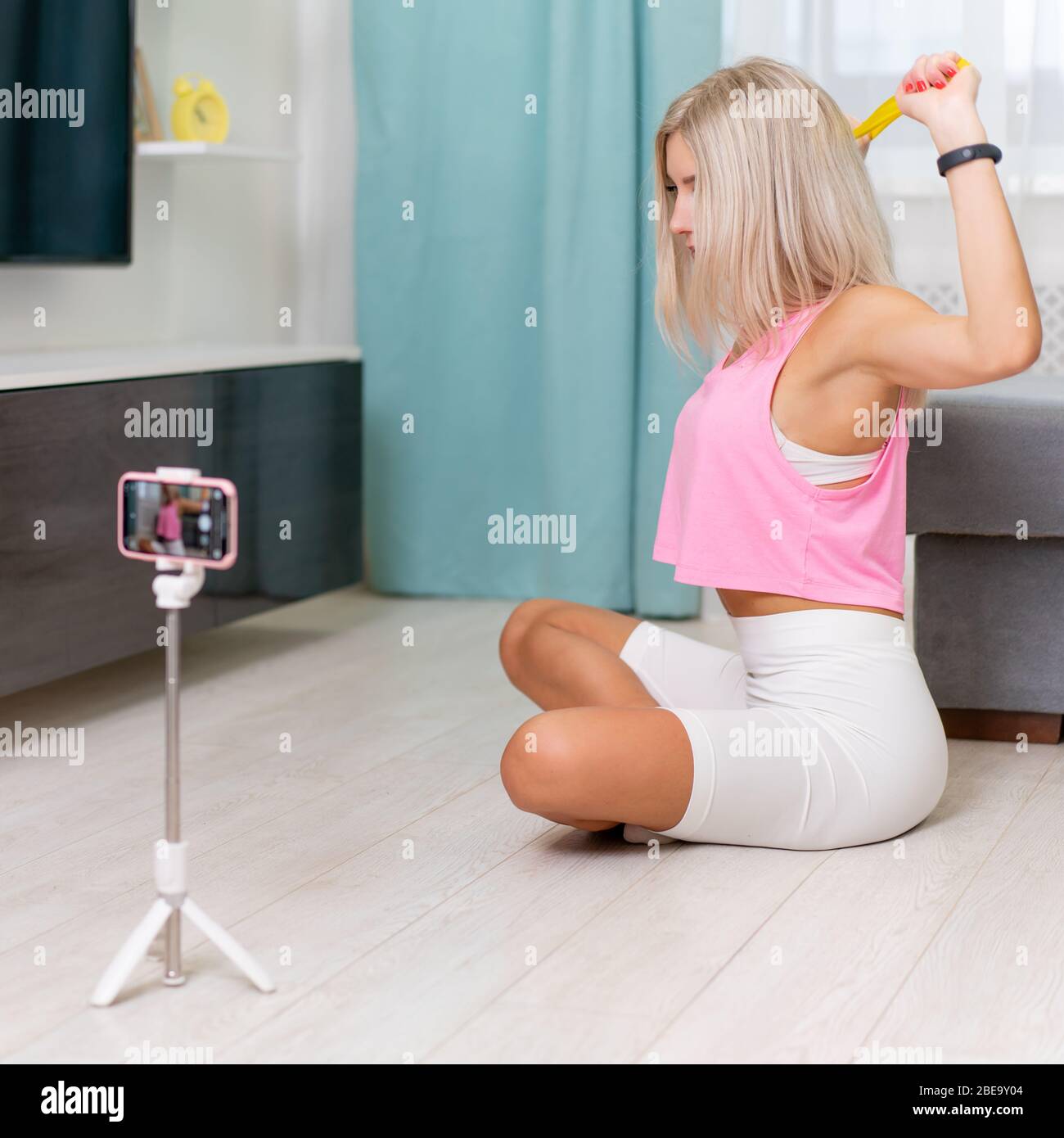 Blonde woman blogger making online broadcast, learning how to make exercize with bands at home. Social media star Stock Photo