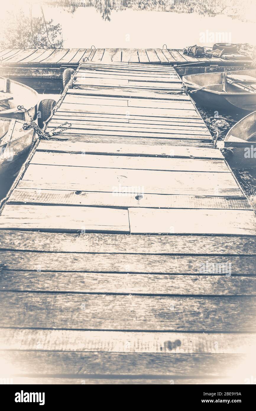 Old vintage photo. Old wooden pier and several boats Stock Photo - Alamy