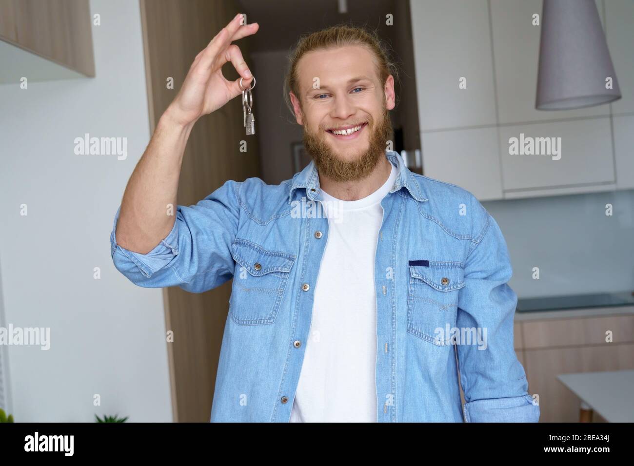Smiling proud young man renter first time estate owner holding key to new home. Stock Photo