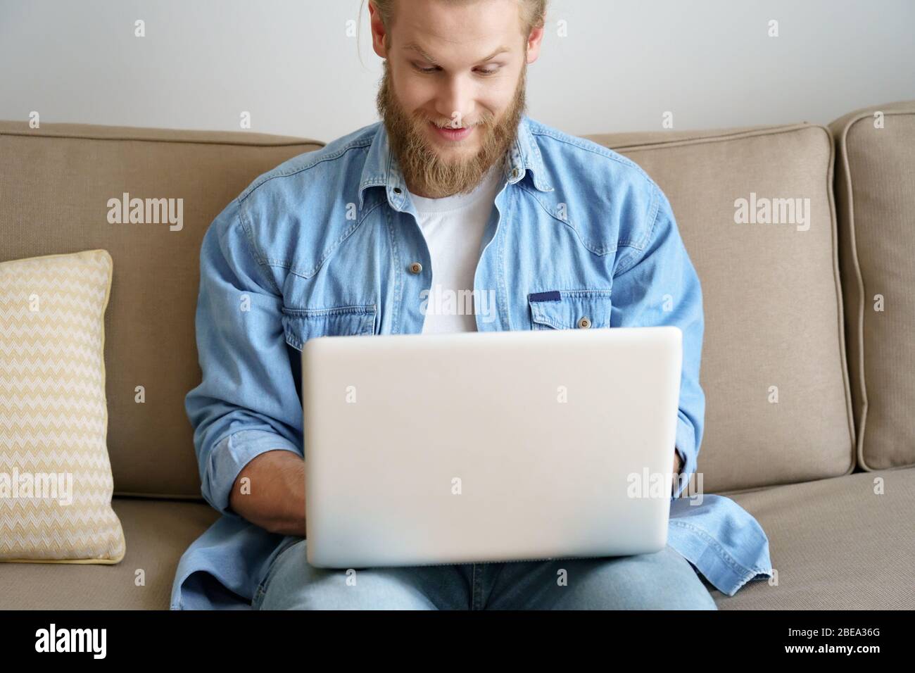 Surprised man computer user winning online sport betting using laptop on sofa. Stock Photo