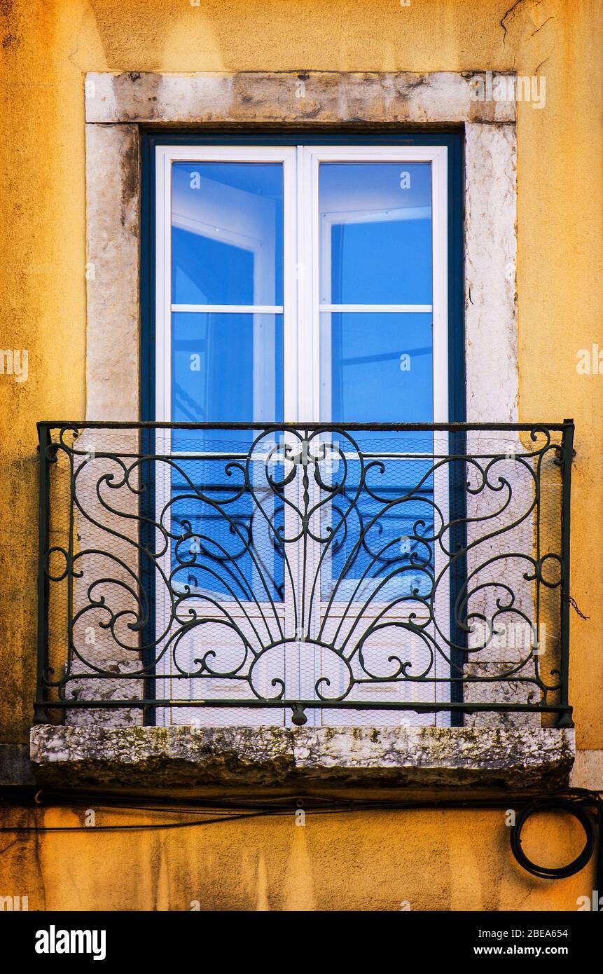 Old and damaged window with iron balcony in a yellow wall Stock Photo