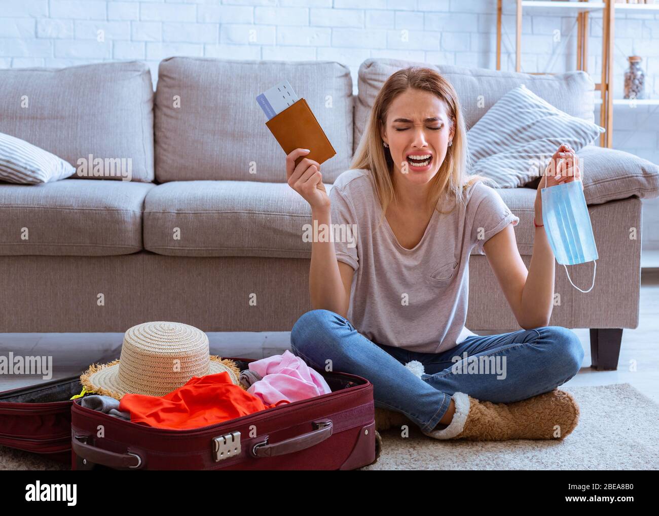 Woman crying at home with protective mask and passport in hands Stock Photo