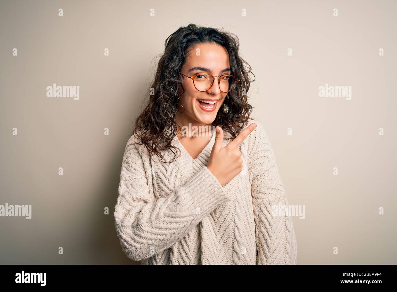 Beautiful woman with curly hair wearing casual sweater and glasses over ...