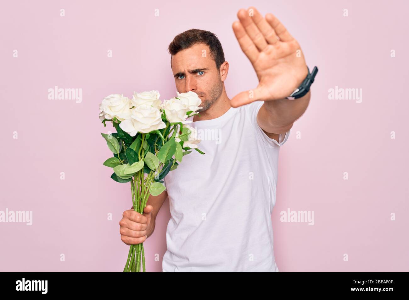 Young handsome man with blue eyes holding bouquet of flowers over pink ...