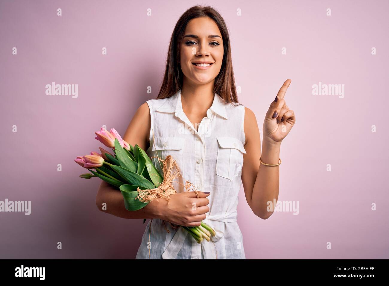 Young beautiful brunette woman holding bouquet of tulips flowers over ...