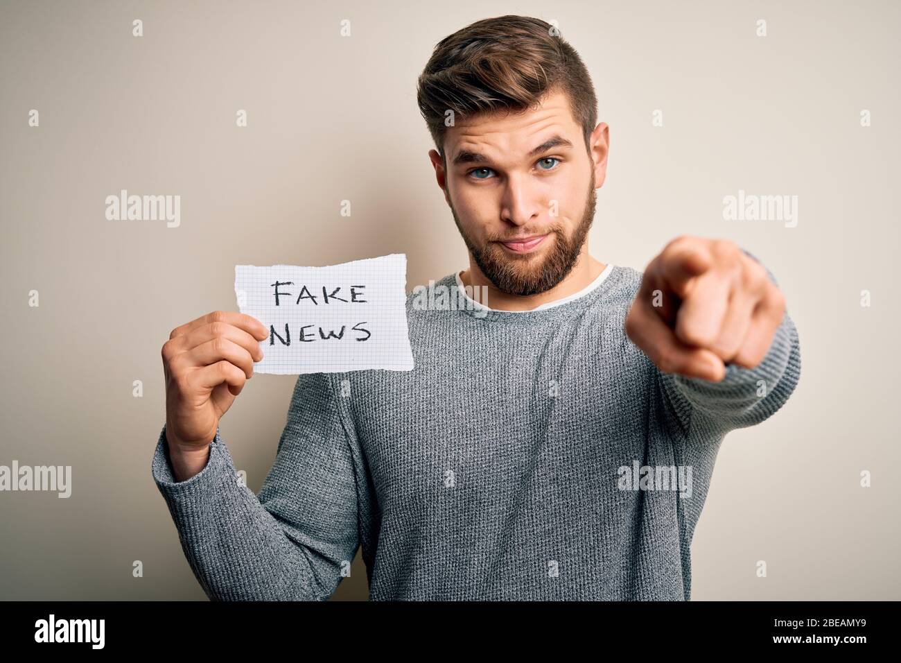 Young blond man with beard and blue eyes holding paper with fake news ...