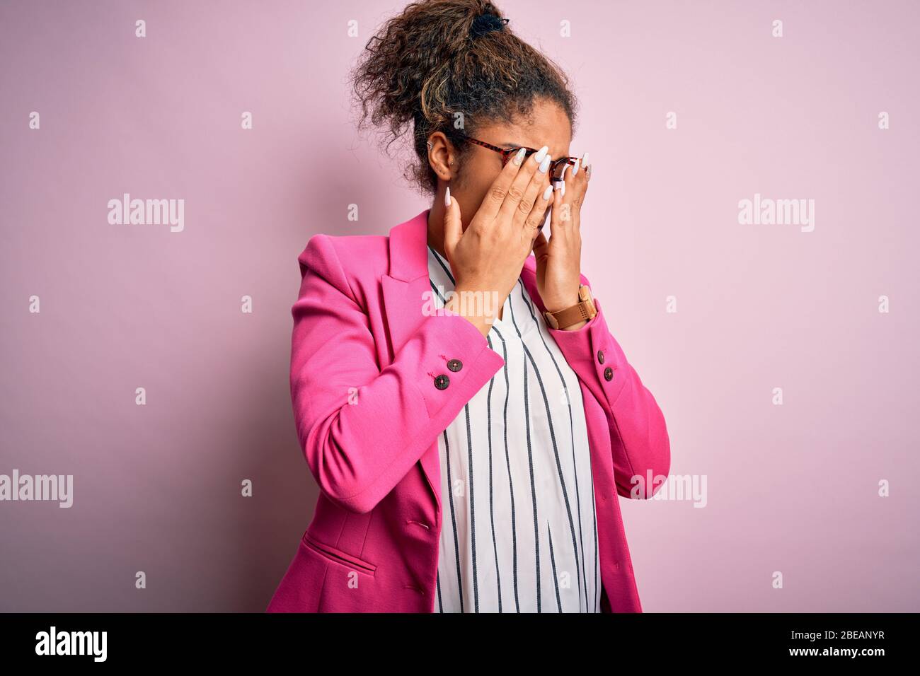 Beautiful african american businesswoman wearing jacket and glasses over pink background rubbing eyes for fatigue and headache, sleepy and tired expre Stock Photo
