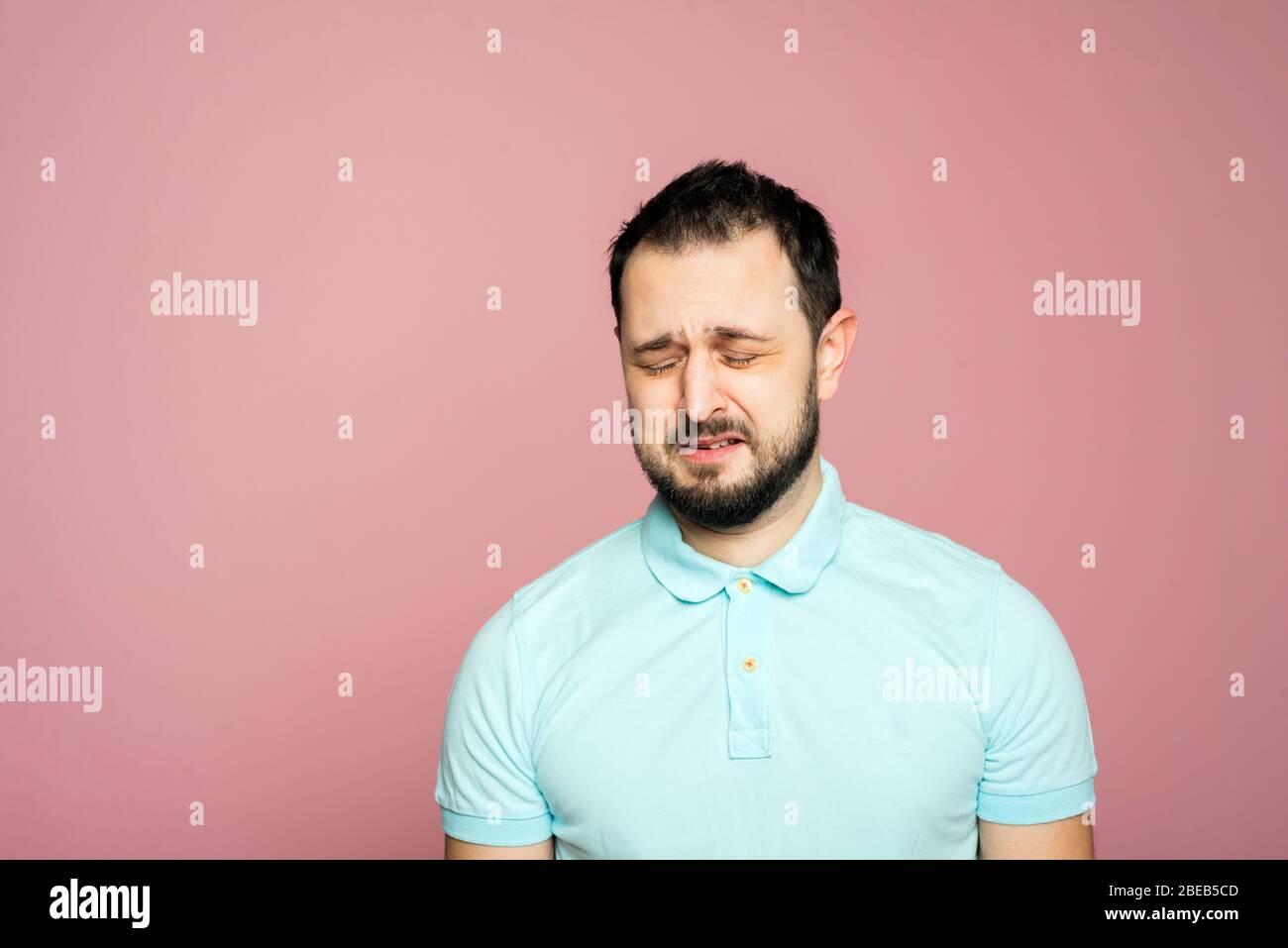 A face of a bearded man on the pink background. Crying man is sad and ...