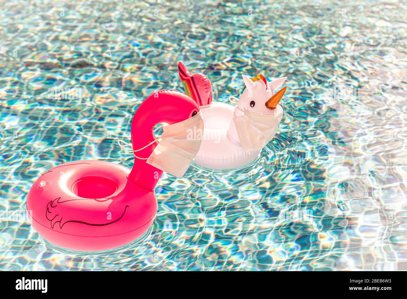 Swimming pool toys unicorn and flamingo in a medical face mask. Concept of Coronavirus outbreak impact on a travel industry for summer season 2020 Stock Photo