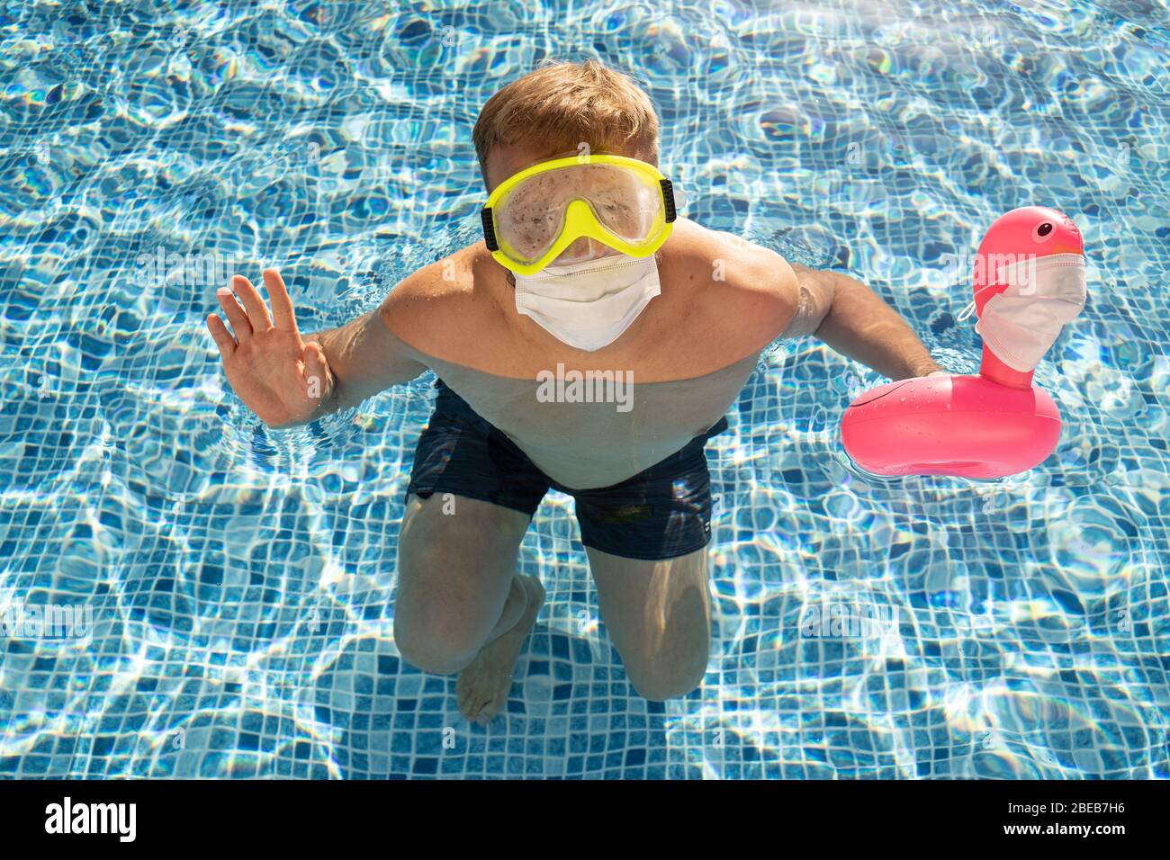 Caucasian white male in swimming pool with a toy flamingo in a medical face mask. Concept of Coronavirus outbreak impact on a travel industry for summ Stock Photo