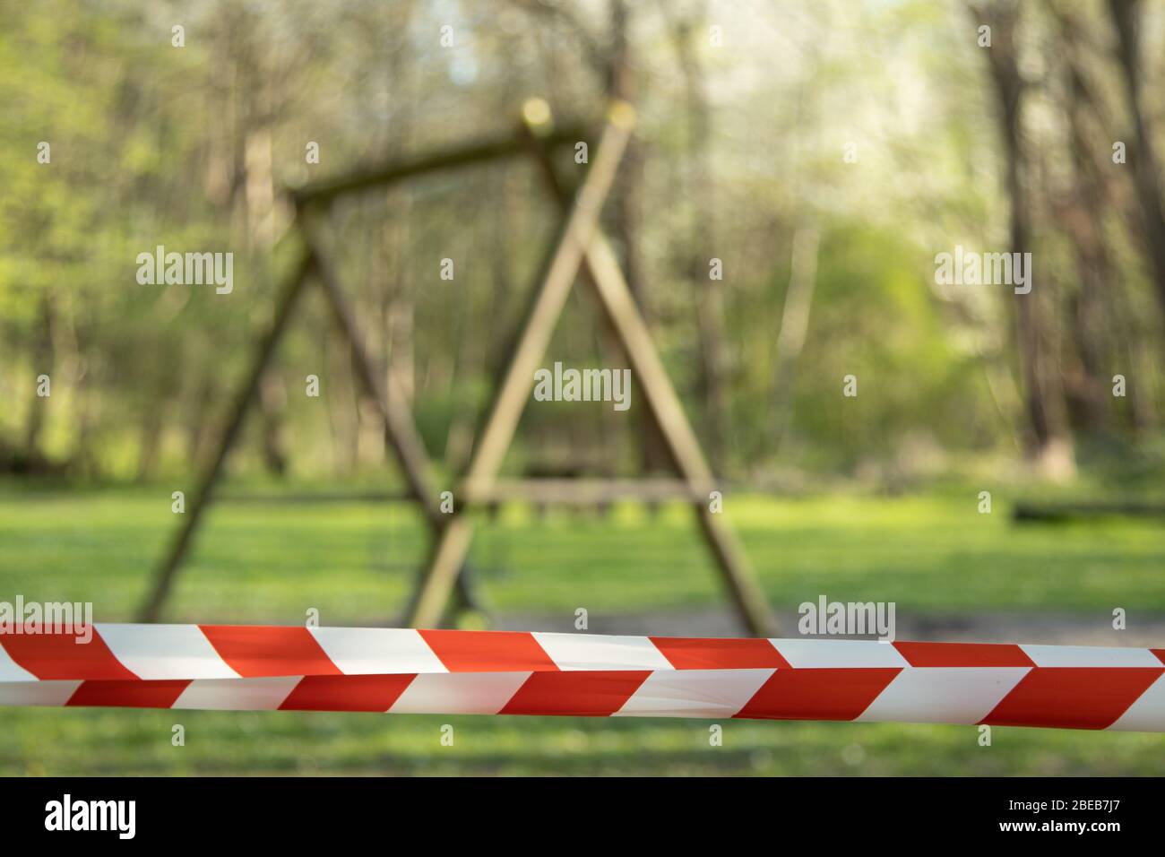 cordoned off playground with children's swing, surroundet by trees, forcus on barrier tape Stock Photo