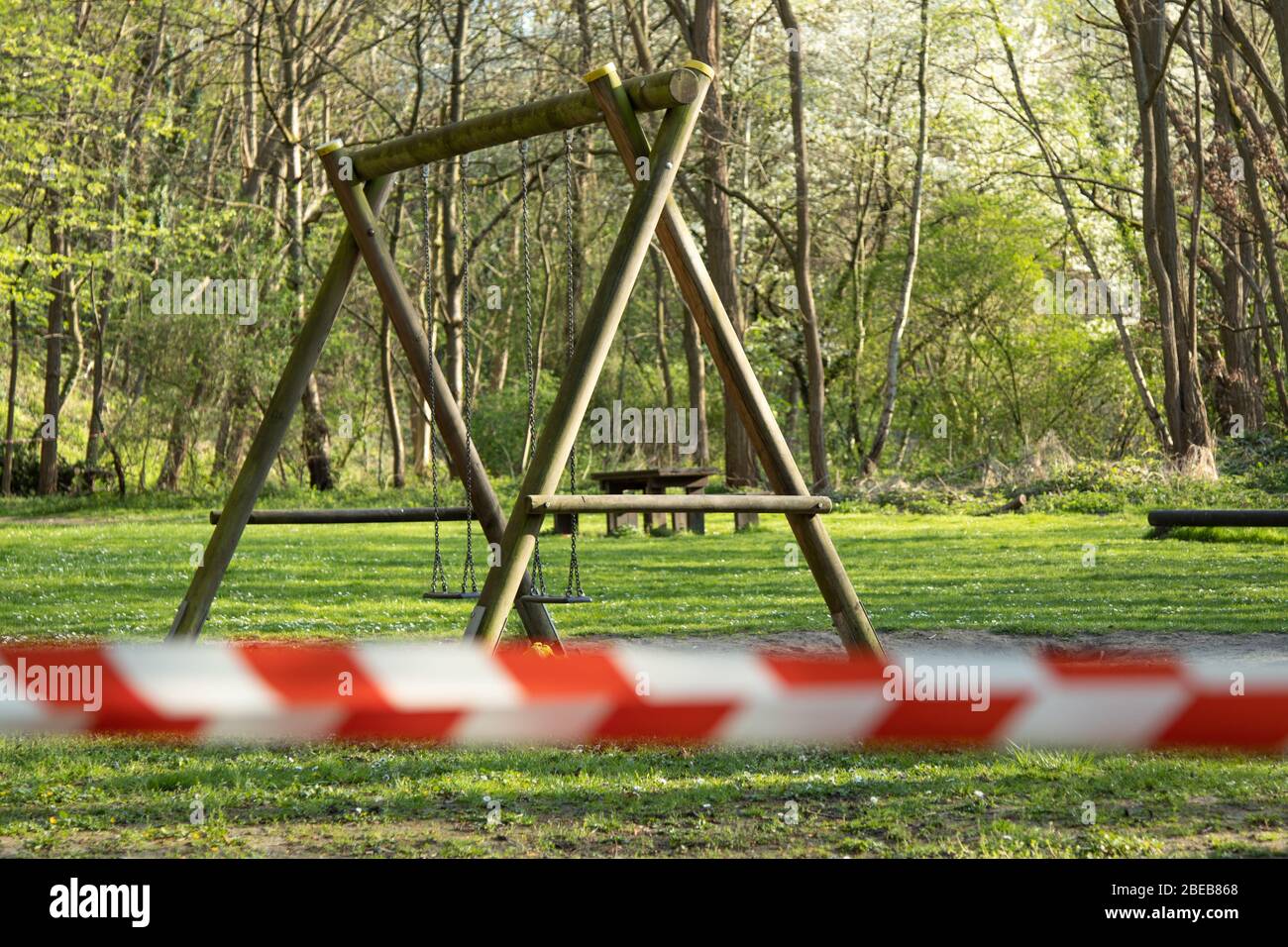 cordoned off playground with children's swing, surroundet by trees, forcus on background, blurred barrier tape Stock Photo