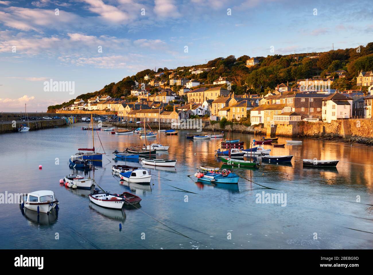 Morning sun lighting up the cottages along the waterfront of Mousehole harbour, the picturesque cornish village situated in West Cornwall Stock Photo