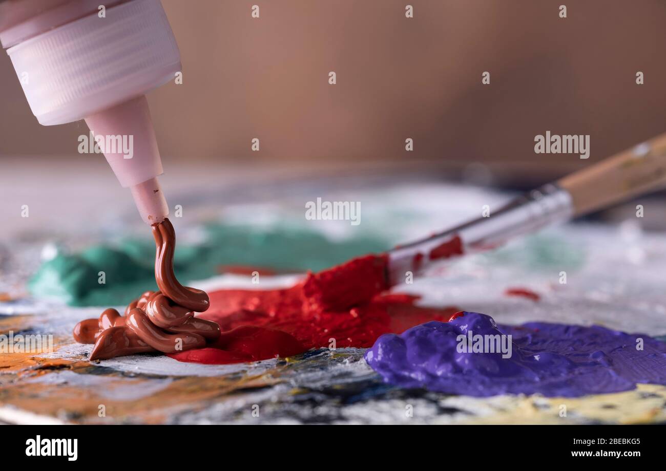 Creative artist using paintbrush to mix green and red oil paint on colorful palette. Stock Photo