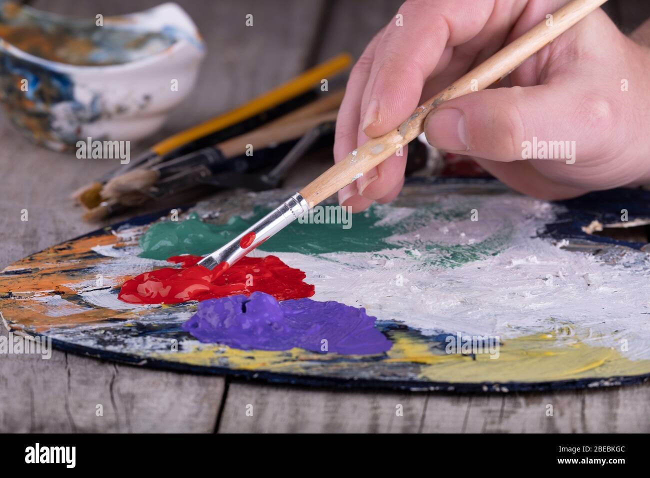 Fine art school. Closeup of wooden palette with acrylic paint and paintbrush in artist hands. Stock Photo
