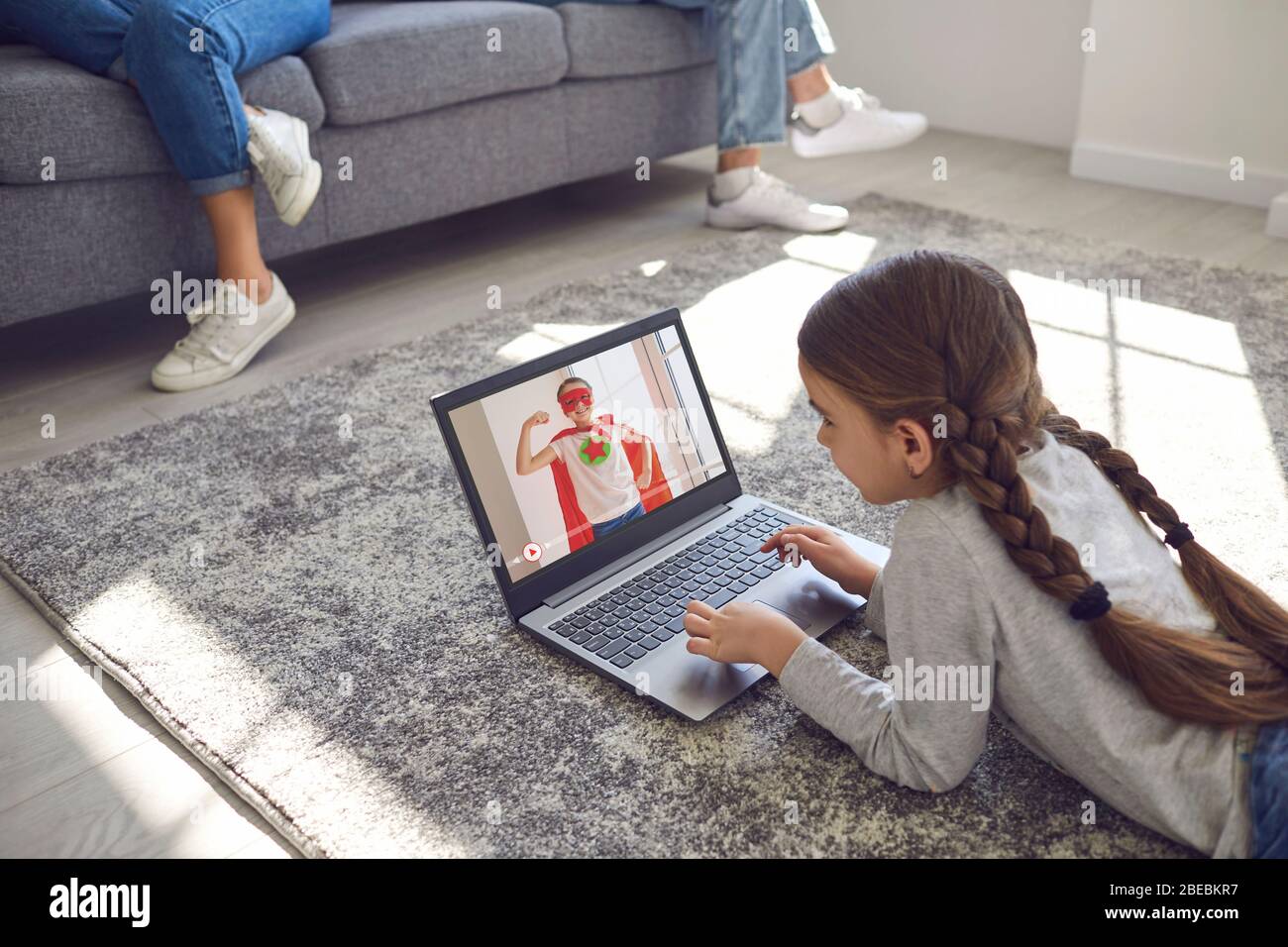 Girl child watching online video game entertainment lying comfortably on the floor in a room with family at home. Stock Photo