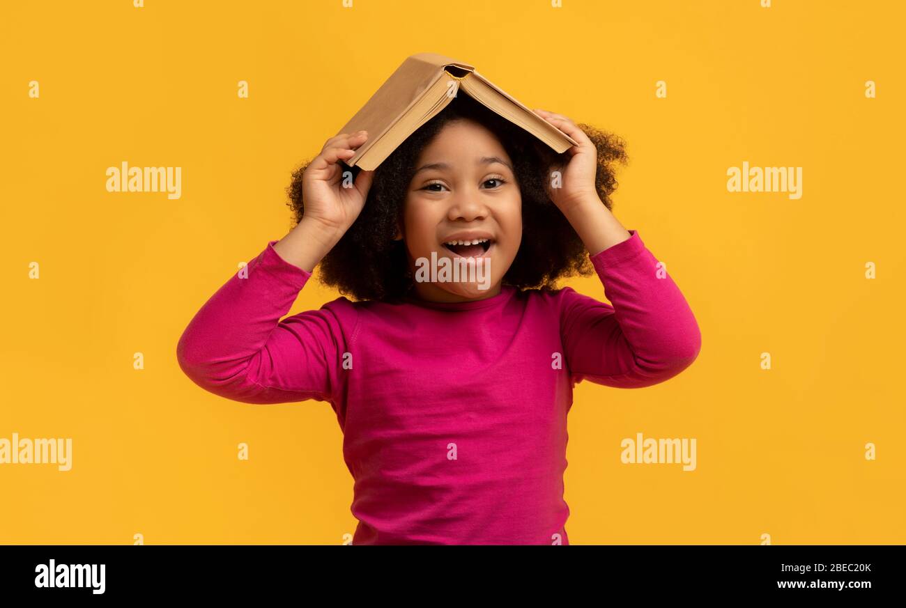 Positive Black Little Girl Holding Opened Book On Her Head Stock Photo ...