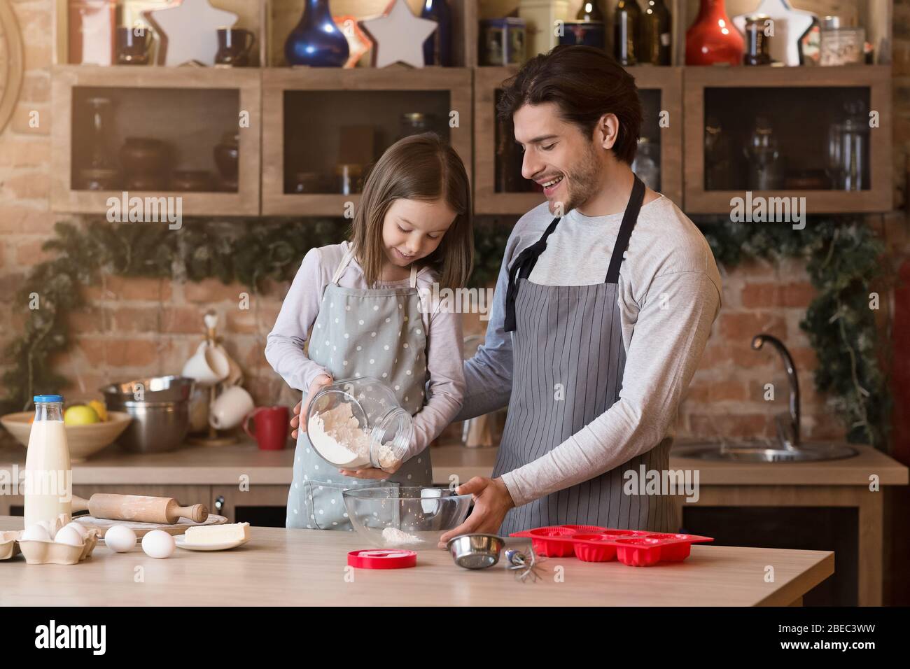 Little girl helping her father to bake, adding flour to bowl Stock Photo
