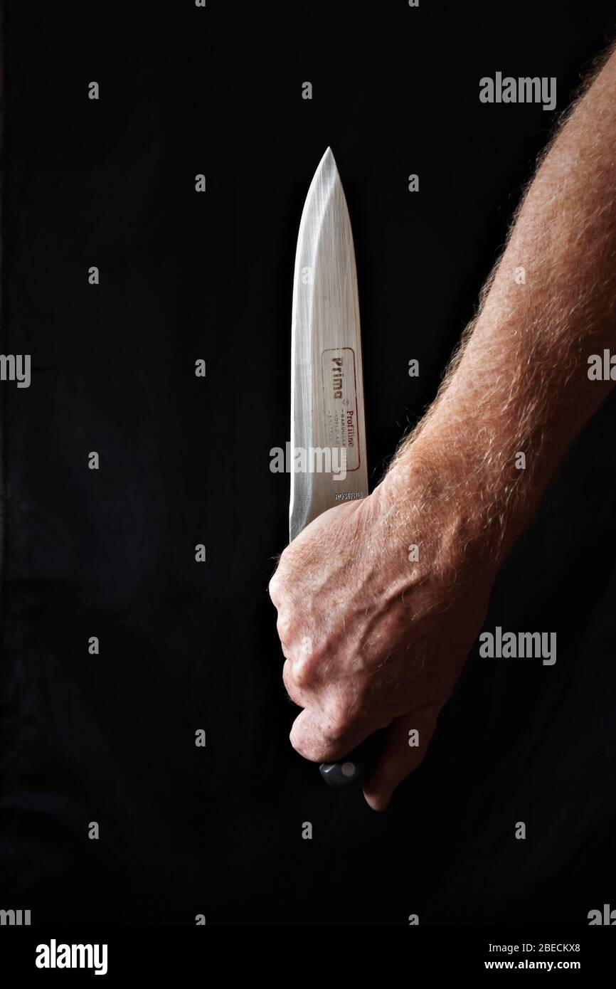 close up of hand holding a kitchen carving knife against a black background Stock Photo